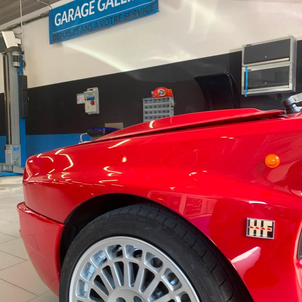Avant d'une Lancia Delta Integrale rouge et sa jante alliage, dans l'atelier